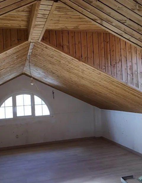 Buhardilla con la estructura de la cubierta en madera vista y ventana en arco
